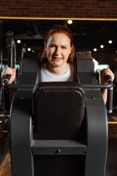 Chica con sobrepeso intencional haciendo ejercicio de extensión de brazos en la máquina de fitness - foto de stock