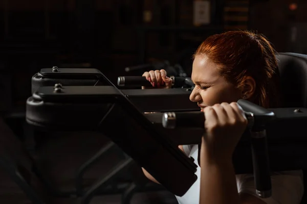 Purposeful overweight girl doing arms extension exercise on fitness machine — Stock Photo