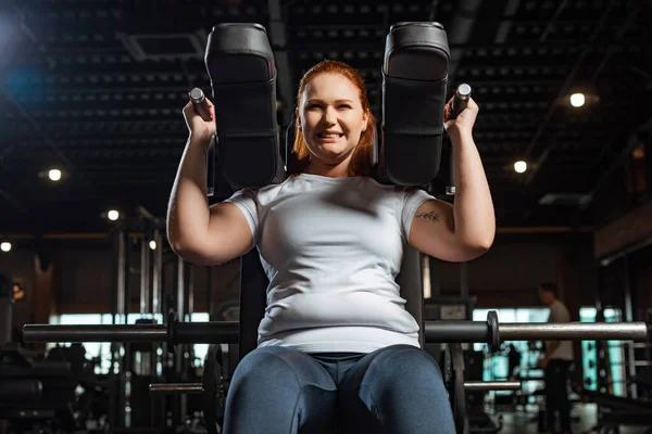 Vista ritagliata di intenzionale ragazza in sovrappeso che fa esercizio di estensione delle braccia sulla macchina per il fitness — Foto stock