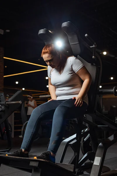 Chica con sobrepeso en entrenamiento de ropa deportiva en la máquina de fitness en el gimnasio - foto de stock