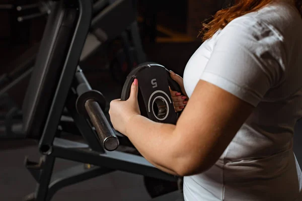 Vue recadrée de la fille en surpoids prenant le disque de poids de la machine de fitness — Photo de stock