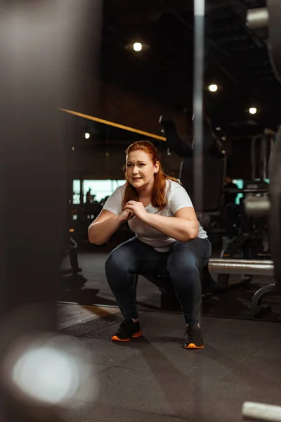 Selective focus of overweight girl squatting with clenched hands in gym — Stock Photo