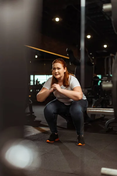 Enfoque selectivo de chica con sobrepeso en cuclillas con las manos apretadas en el gimnasio - foto de stock