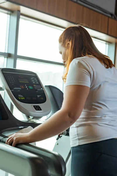 Redhead overweight girl working out on treadmill in gym near window — Stock Photo