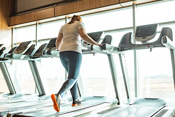 Chica con sobrepeso haciendo ejercicio en la cinta de correr en el gimnasio contra ventana - foto de stock