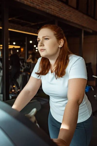 Pensive overweight girl training on treadmill in gym — Stock Photo