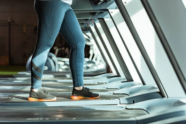 Vista cortada de menina com sobrepeso em leggings correndo em esteira na academia — Fotografia de Stock