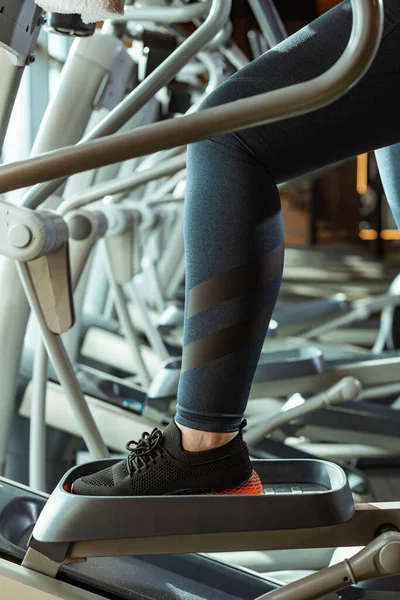 Vue recadrée de la fille en surpoids dans les leggings formation sur stepper dans la salle de gym — Photo de stock