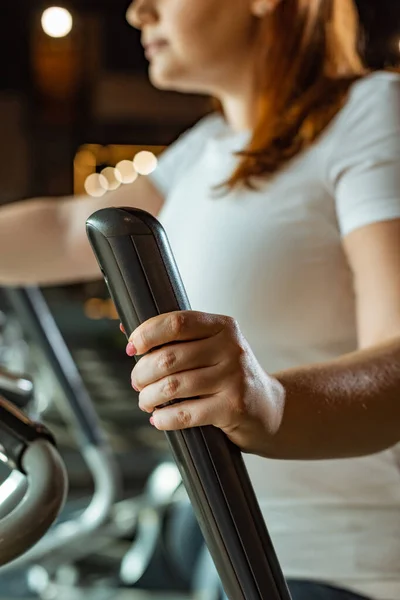 Vista parcial de la chica con sobrepeso haciendo ejercicio en la máquina de paso en el gimnasio - foto de stock