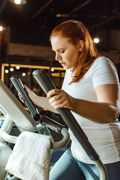 Centrado entrenamiento de chica con sobrepeso en la máquina paso a paso en el gimnasio - foto de stock