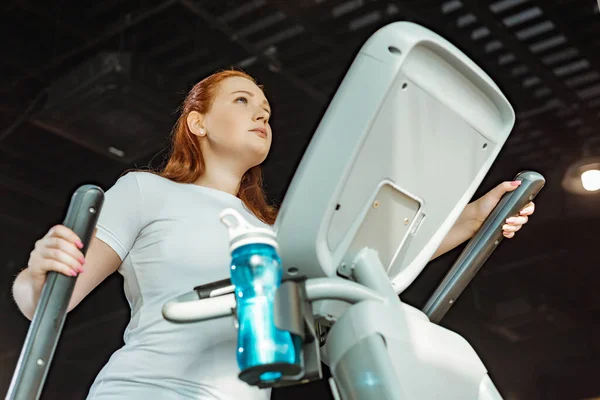 Niedrige Blickwinkel auf fokussierte übergewichtige Mädchen, die im Fitnessstudio auf Stepper trainieren — Stockfoto