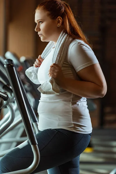 Entrenamiento de niña con sobrepeso seguro en la máquina de paso mientras sostiene la toalla - foto de stock