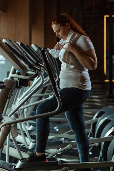 Side view of focused overweight girl training on stepper while holding towel — Stock Photo