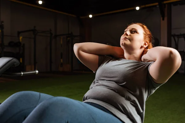 Pretty, overweight girl doing abs with hands behind head in gym — Stock Photo