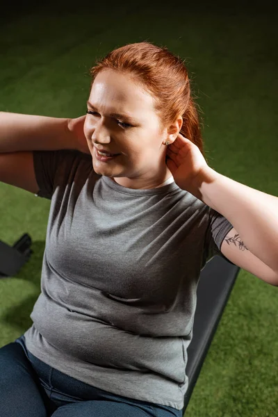Высокий угол зрения целеустремленной девушки с избыточным весом делать упражнения абс на тренажере — стоковое фото