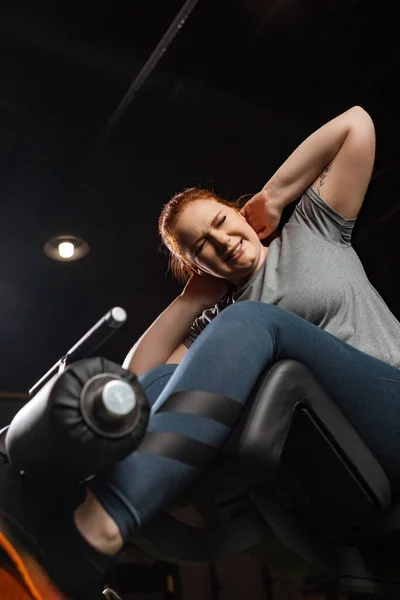 Vista de ángulo bajo de la chica con sobrepeso intencional haciendo ejercicio abdominales en la máquina de fitness - foto de stock