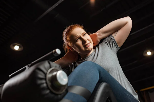 Низкий угол зрения целеустремленной девушки с избыточным весом делать упражнения ABS на тренажере — стоковое фото