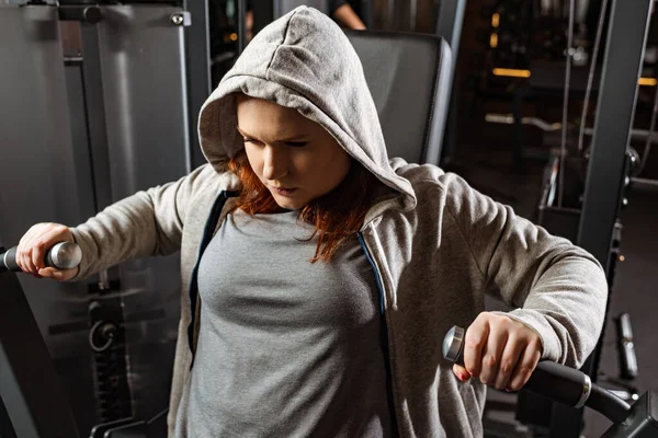 Chica con sobrepeso concentrado haciendo ejercicio de extensión de brazos en la máquina de fitness - foto de stock