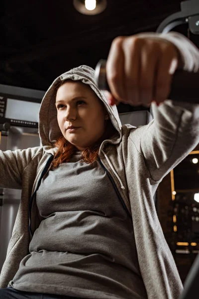 Selektiver Fokus eines konzentrierten übergewichtigen Mädchens, das Armstreckübungen an einem Fitnessgerät macht — Stockfoto