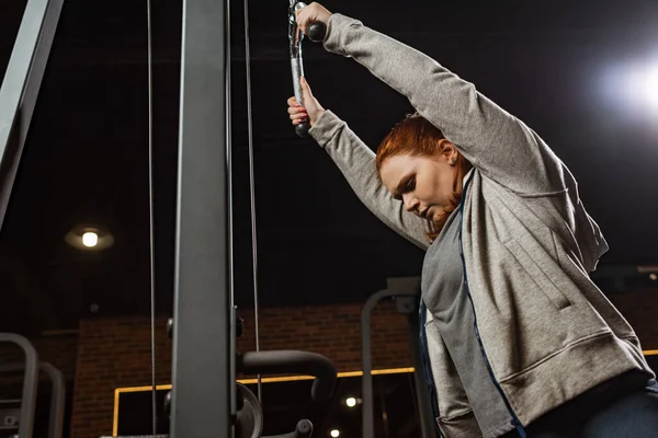 Concentrée fille en surpoids faisant exercice d'extension des bras sur la machine de remise en forme — Photo de stock