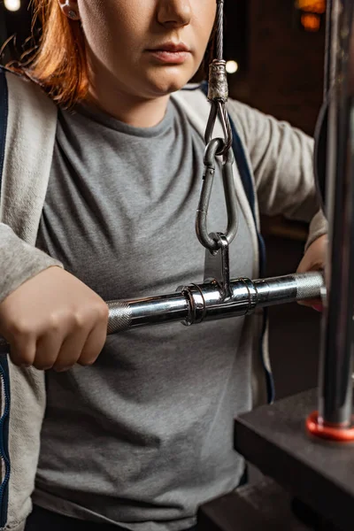 Cropped view of overweight girl doing arms extension exercise on fitness machine — Stock Photo