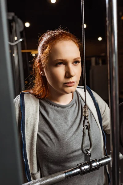 Selective focus of confident overweight girl doing arms extension exercise on training machine — Stock Photo