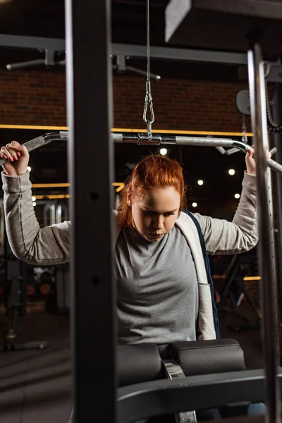 Selective focus of overweight girl doing arms extension exercise on training machine — Stock Photo