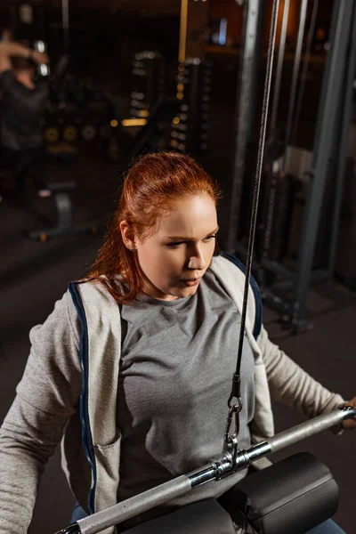 Chica con sobrepeso concentrado haciendo ejercicio de extensión de brazos en la máquina de fitness - foto de stock