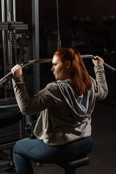 Confident overweight girl doing arms extension exercise on fitness machine — Stock Photo