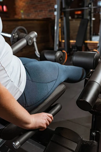Cropped view of overweight girl doing leg extension exercise on fitness machine — Stock Photo