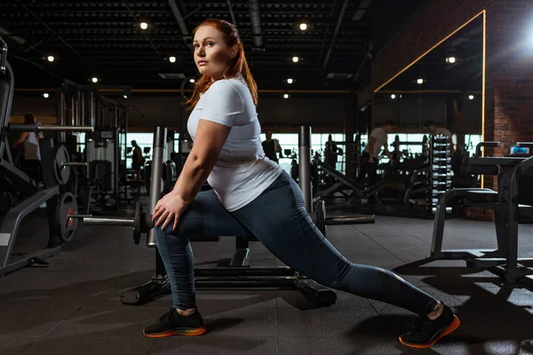 Pretty, overweight girl doing lounges exercise in gym — Stock Photo