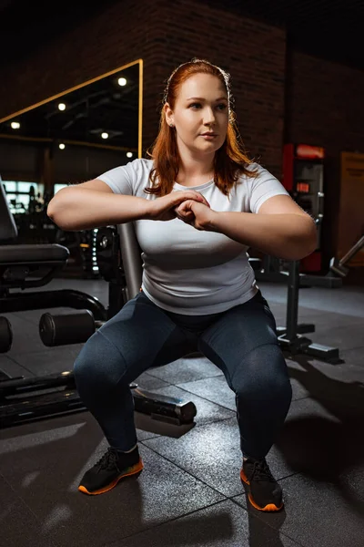 Centrado chica con sobrepeso en cuclillas con las manos apretadas en el gimnasio - foto de stock