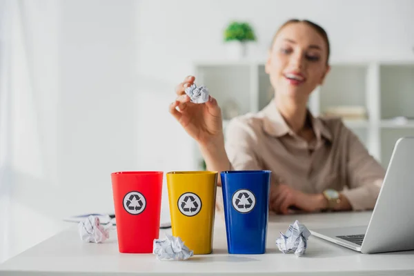 Selective focus of happy businesswoman throwing crumpled papers into recycling buckets in office — Stock Photo