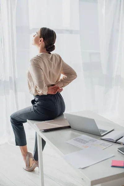 Mujer de negocios cansado que se extiende de nuevo en el lugar de trabajo con el ordenador portátil - foto de stock