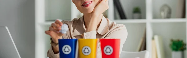 Panoramic shot of smiling businesswoman throwing crumpled paper into recycling buckets — Stock Photo