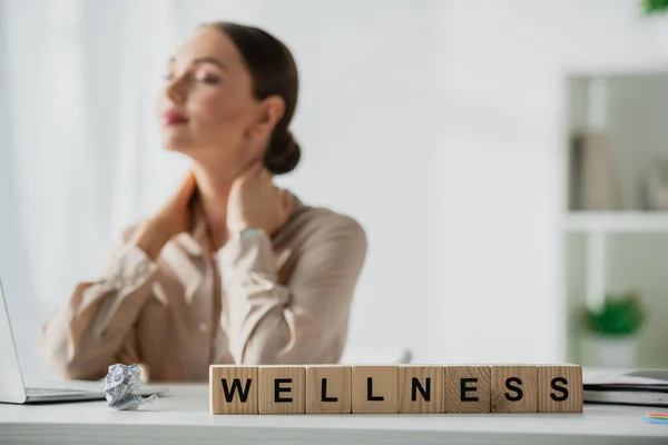 Selective focus of businesswoman resting at workplace with laptop and alphabet cubes with wellness word — Stock Photo