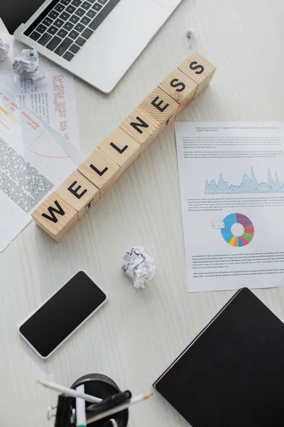 Top view of business workplace with documents, laptop, smartphone and alphabet cubes with wellness word — Stock Photo