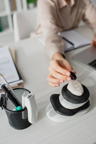 Cropped view of businesswoman working with laptop at workplace with zen stones — Stock Photo