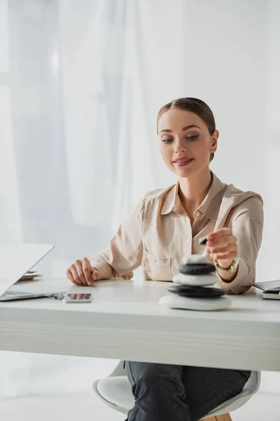 Attrayant femme d'affaires assis sur le lieu de travail avec des pierres zen et ordinateur portable — Photo de stock