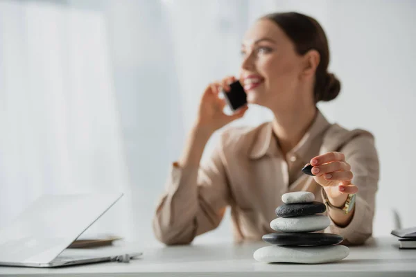 Selektiver Fokus der Geschäftsfrau, die am Arbeitsplatz mit Zen-Steinen auf dem Smartphone spricht — Stockfoto