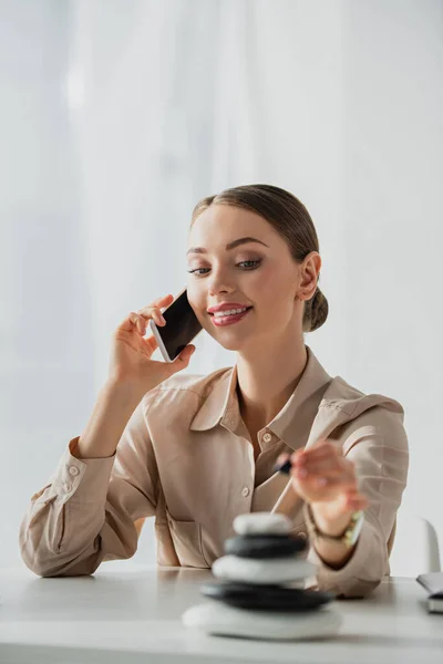 Zufriedene Geschäftsfrau, die am Arbeitsplatz mit Zen-Steinen auf dem Smartphone spricht — Stockfoto