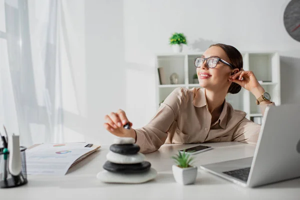 Femme d'affaires rêveuse assis sur le lieu de travail avec des pierres zen et ordinateur portable — Photo de stock