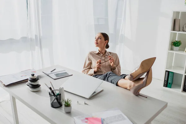 Attractive young businesswoman procrastinating at workplace with laptop and feet on table — Stock Photo