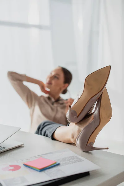 Selective focus of young businesswoman procrastinating with feet on table in office — Stock Photo