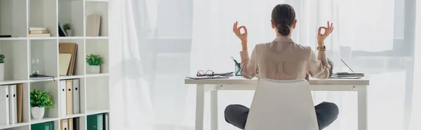 Panoramaaufnahme einer Geschäftsfrau beim Meditieren in Lotus-Pose mit Gyan Mudra am Arbeitsplatz mit Räucherstäbchen — Stockfoto