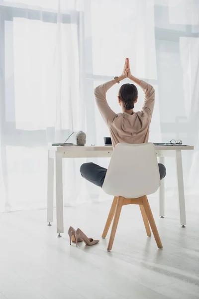 Vista posterior de la mujer de negocios meditando con gesto namaste en el lugar de trabajo con varilla de incienso - foto de stock