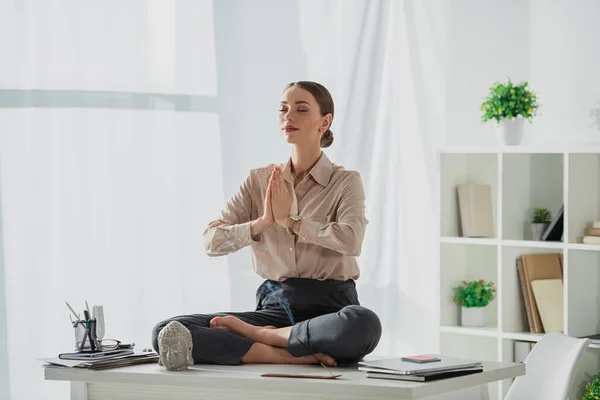 Femme d'affaires entreprise méditant dans la pose de lotus avec geste namaste sur le lieu de travail avec tête de Bouddha et bâton d'encens — Photo de stock