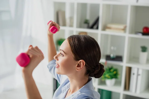 Beautiful happy businesswoman training with dumbbells in office — Stock Photo