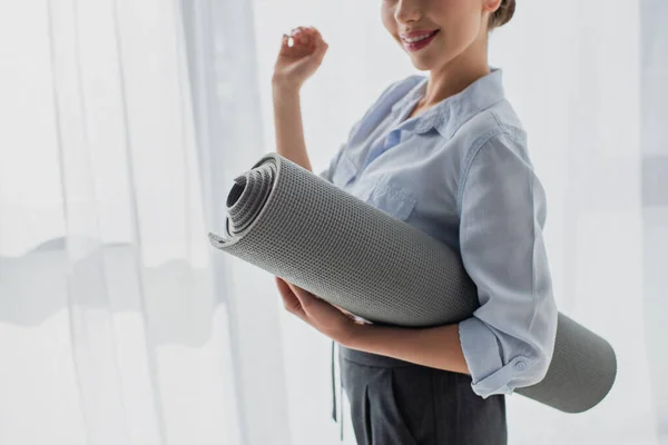 Vista ritagliata di sorridere giovane donna d'affari in possesso di tappetino fitness in ufficio — Foto stock