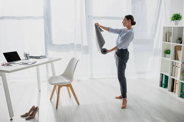 Bela jovem empresária segurando tapete de ioga no escritório — Fotografia de Stock